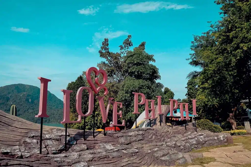 Eine Außeninstallation aus großen, bunten Buchstaben, die „I love Phi Phi“ buchstabieren, mit einer üppigen Landschaft, Bergen und einem klaren Himmel im Hintergrund während eines Segeltörns.