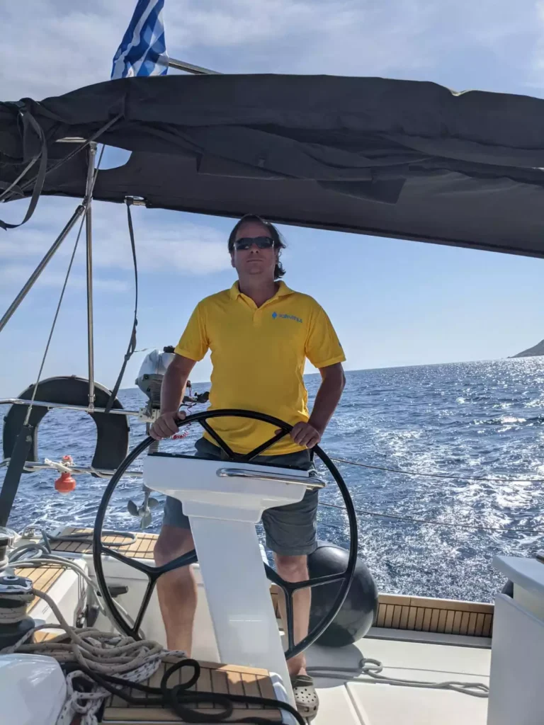 Konzentrierter sailwithus Skipper am Steuer eines Segelboots mit griechischer Flagge – sailwithus segeln griechenland