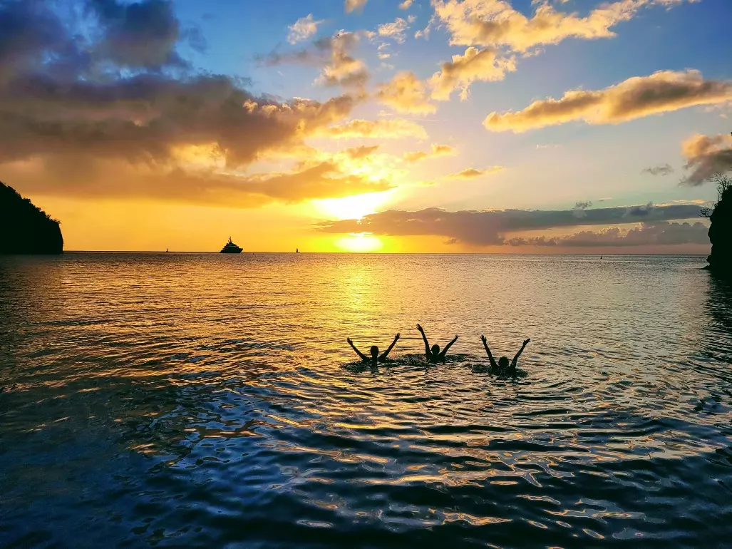 Schwimmer genießen das Wasser bei Sonnenuntergang in der Karibik mit Segelbooten am Horizont.