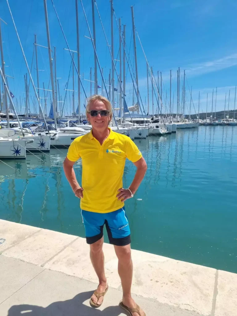 Gut gelaunter sailwithus Skipper im gelben Shirt vor Hafen mit Segelbooten in Trogir – sailwithus kroatien segeltörn