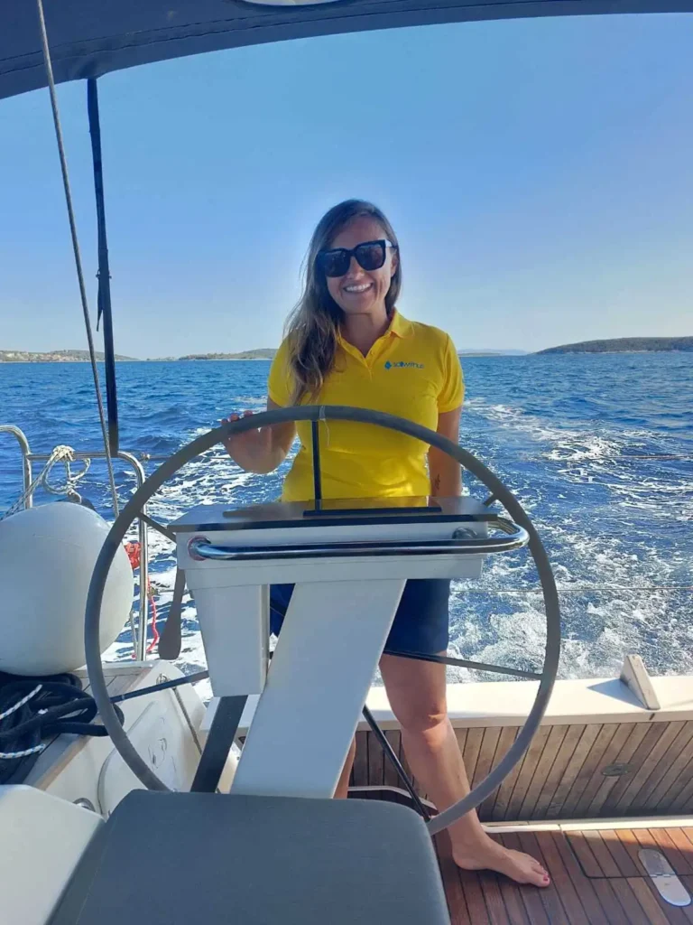 Lächelnde sailwithus Skipperin im gelben Shirt am Steuer in Kroatien – sailwithus segeln kroatien skippertraining