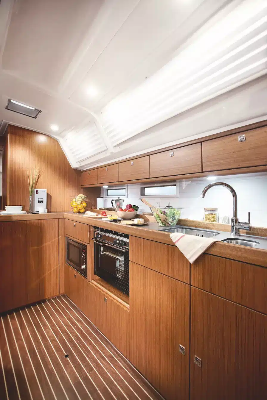 Eine moderne Bootsküche mit eleganten Holzschränken, einer eingebauten Mikrowelle, einem Backofen und einer Edelstahlspüle. Der Boden ist mit horizontalen Holzdielen ausgelegt, was das luxuriöse Gefühl verstärkt, perfekt für