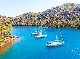 Drei Segelboote ankerten in einer ruhigen türkisfarbenen Bucht, umgeben von üppigen grünen Hügeln unter einem klaren blauen Himmel.