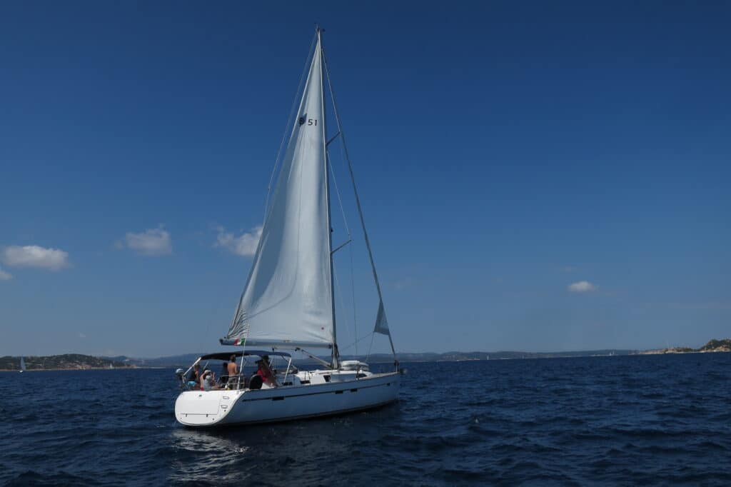 Eine Segelreise mit einer Gruppe von Menschen an Bord gleitet unter klarem Himmel über das ruhige blaue Wasser.