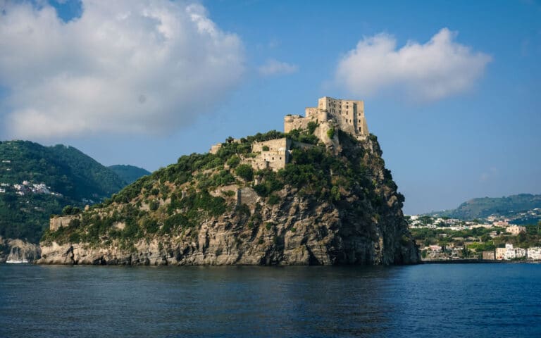 Eine majestätische alte Burg thront auf einer felsigen Insel, umgeben von blauem Wasser, mit einem üppig grünen Hügel im Hintergrund unter einem klaren Himmel während eines Segelyacht-Abenteuers.