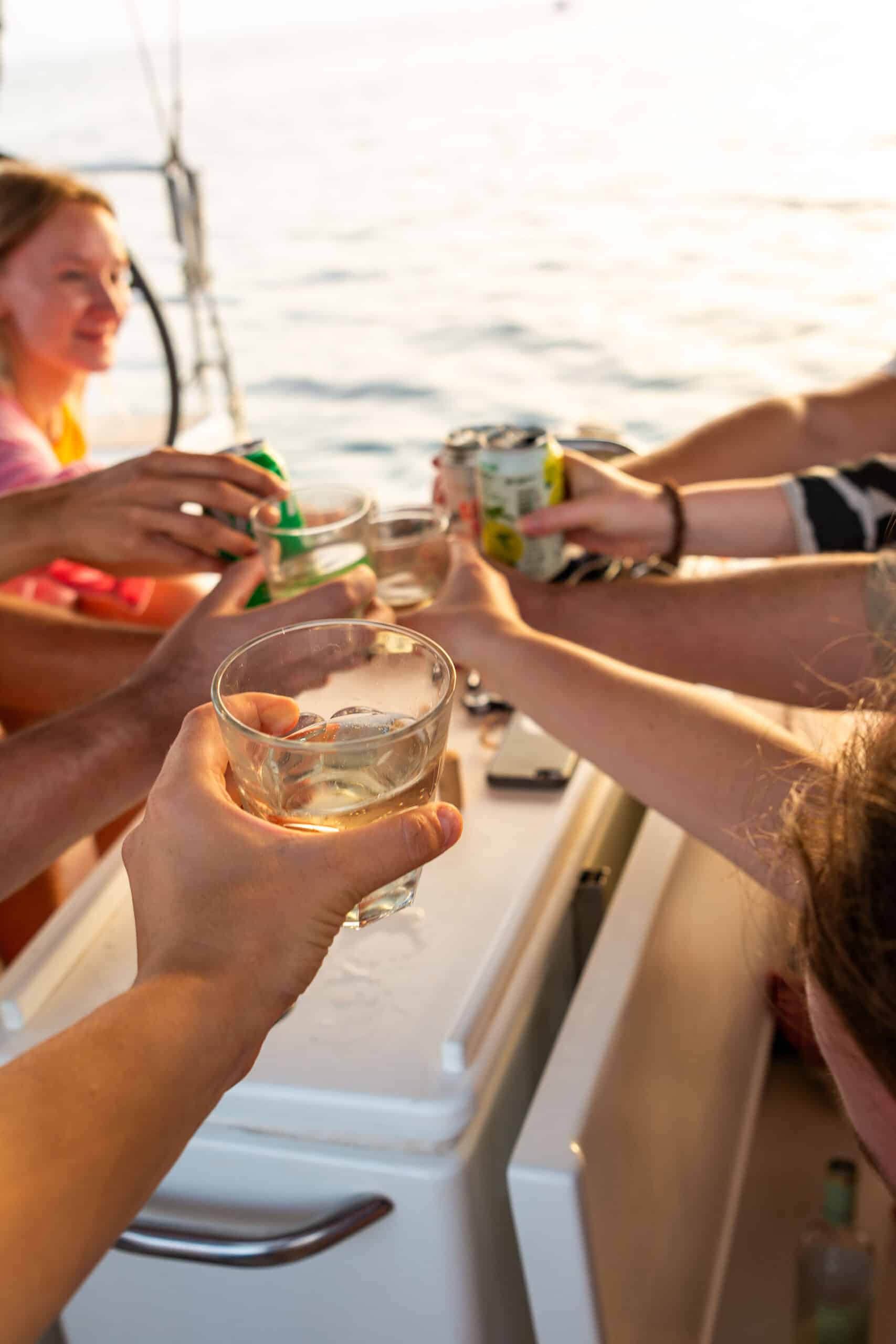Freunde stoßen bei Sonnenuntergang auf einer Segelyacht an und genießen Getränke mit Blick auf das Meer im Hintergrund – ein Zeichen für ein entspanntes geselliges Beisammensein.