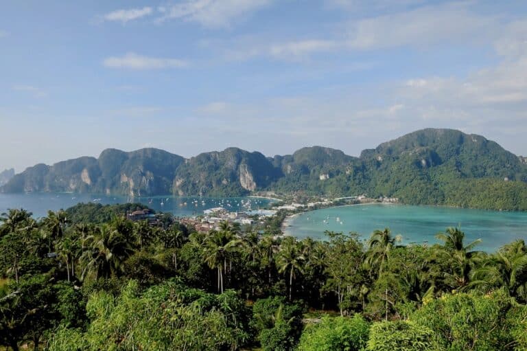 Ein Panoramablick auf eine tropische Küstenstadt mit üppig grünen Hügeln, klarem blauen Wasser und Segelyachten in Küstennähe unter einem strahlend blauen Himmel.