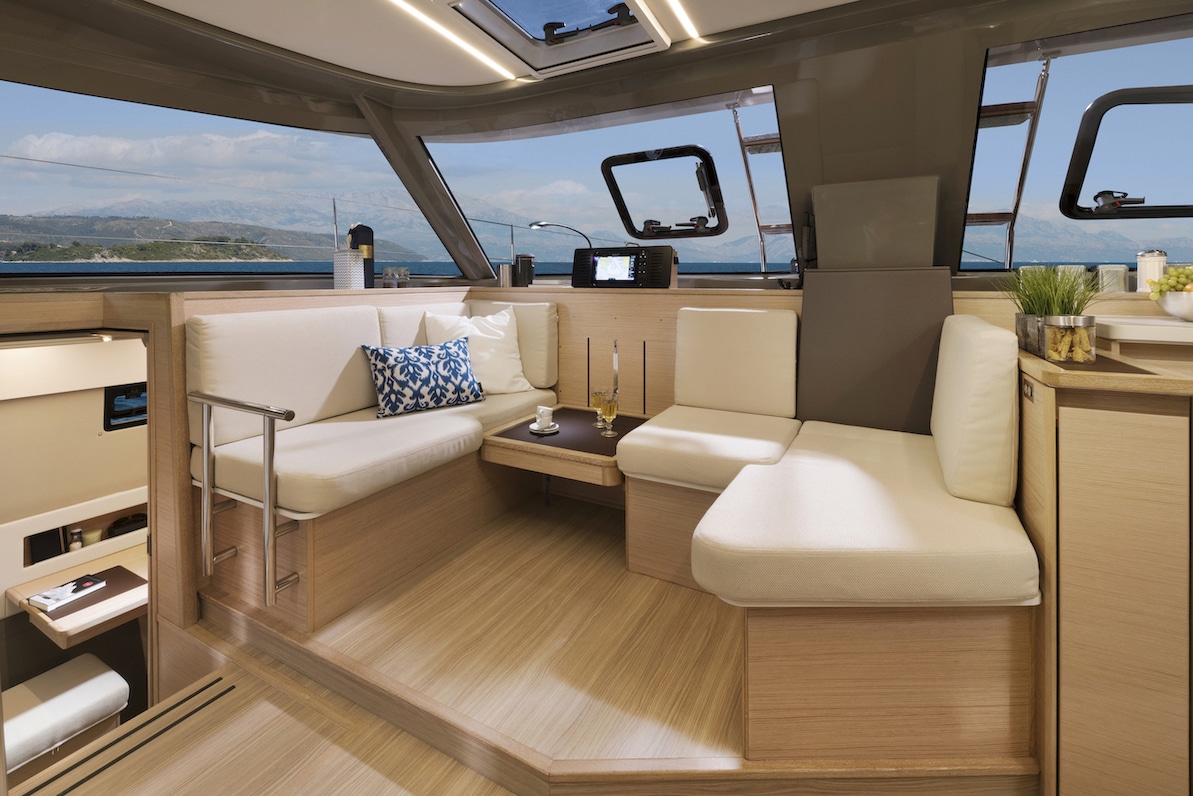 Luxuriöses Segelyacht-Interieur mit einem geräumigen Loungebereich mit cremefarbenen Sofas, poliertem Holzboden und großen Fenstern mit malerischem Meerblick.