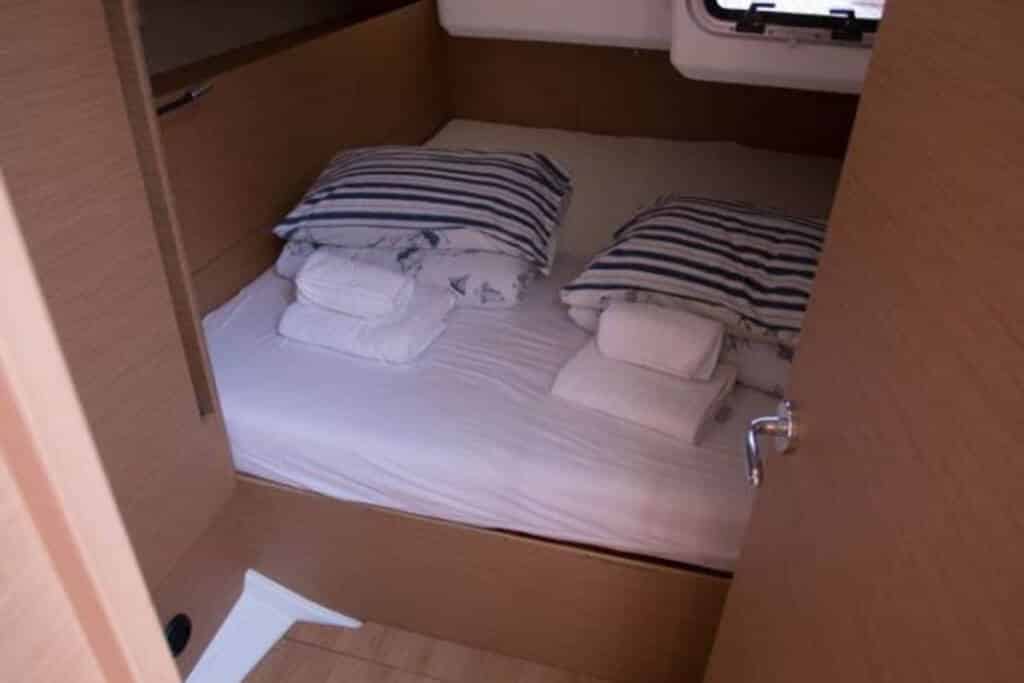 Ein gemütliches Kabinenschlafzimmer auf einer Segelyacht mit einem ordentlich gemachten Bett mit gestreifter Bettwäsche und weißen Handtüchern, umgeben von Holzwänden und Schränken.