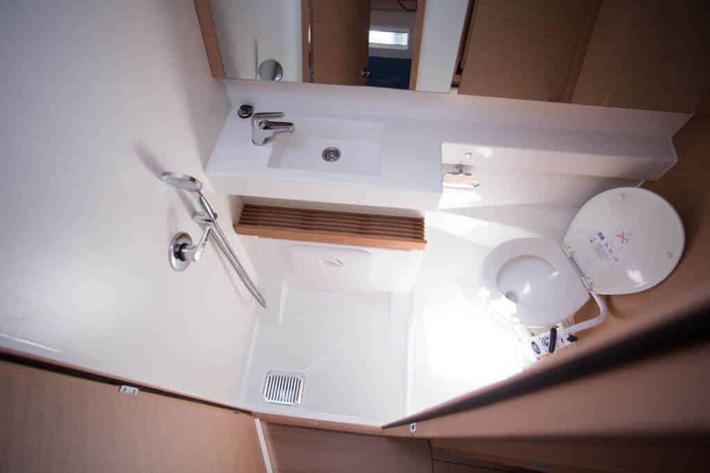 Ein kompaktes Wohnmobilbadezimmer mit weißem Waschbecken, Spiegel, Toilette und Dusche im Spiegel, das die effiziente Nutzung kleiner Räume während einer Segelreise zeigt.