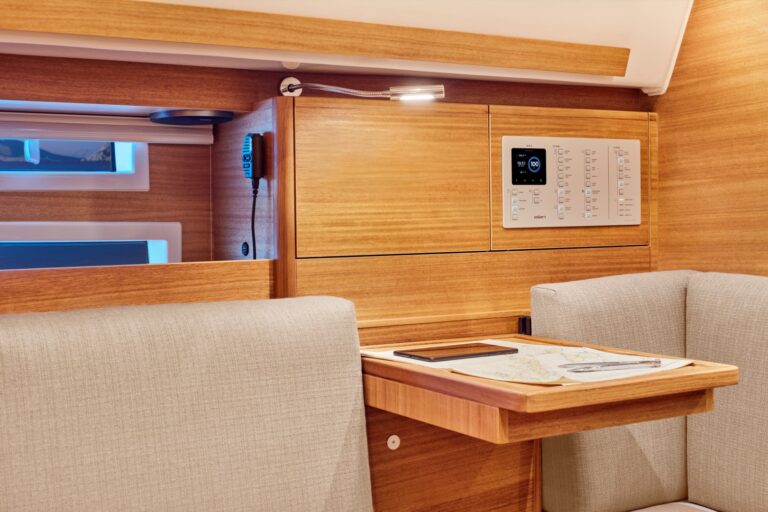 Innenraum einer modernen Segelyacht mit gemütlicher Navigationsstation mit Armaturenbrett aus Holz, elektronischem Bedienfeld und beige gepolsterten Sitzen.
