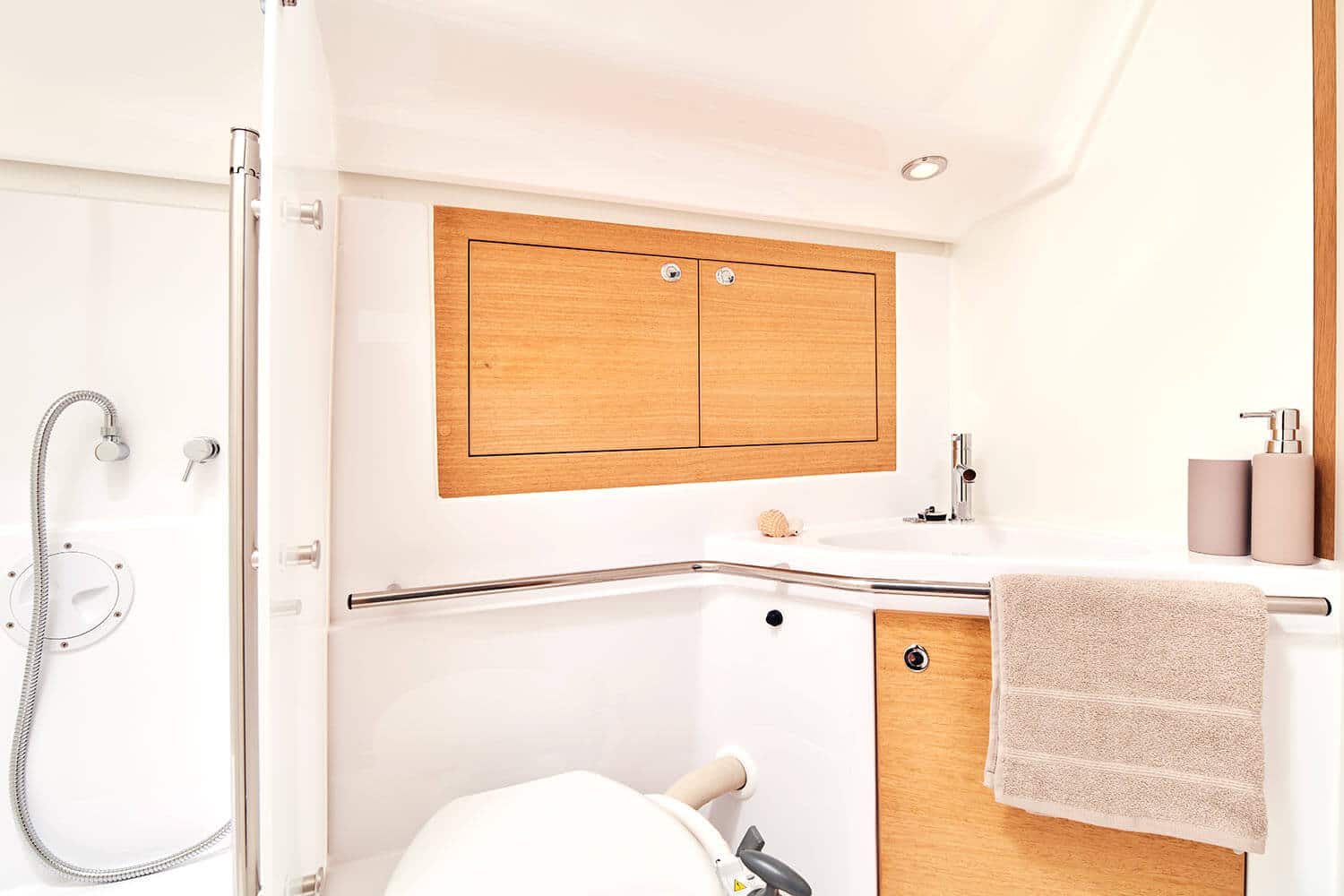 Ein helles, modernes Badezimmer mit einer weißen Toilette, einer beige gefliesten Dusche mit Glastür, Holzschränken und einem weißen Waschbecken mit minimalistischem Dekor im „Segelurlaub“-Stil.