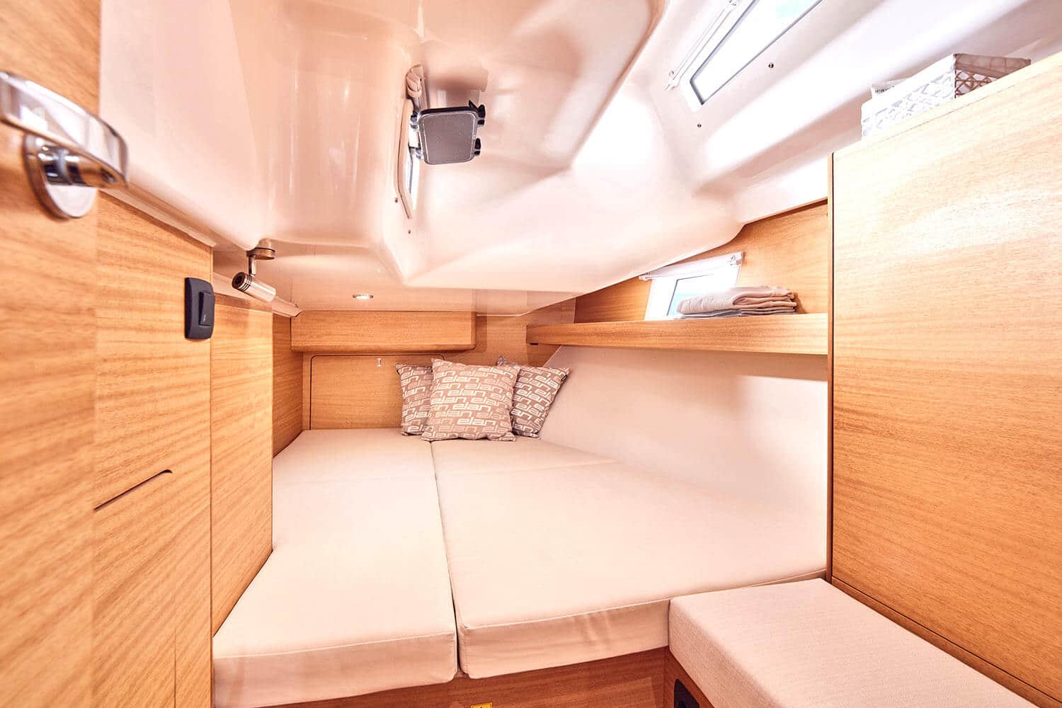 Innenansicht eines modernen Wohnmobils mit gemütlichem Schlafbereich mit gepolstertem Bett, Stauschränken und sanfter Beleuchtung, die an eine Segelyacht erinnert.