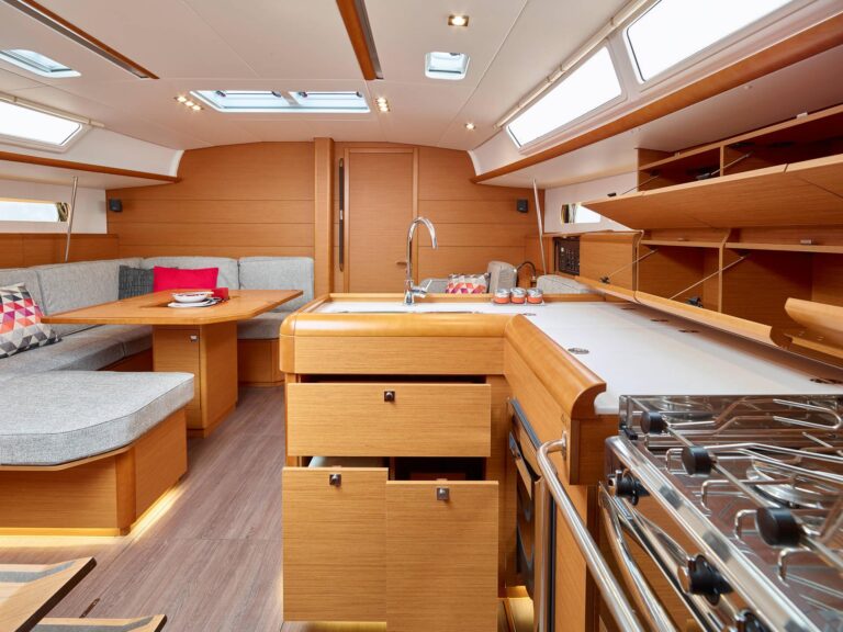 Innenansicht einer modernen Yacht mit gut ausgestatteter Küche mit Holzschränken und Geräten aus Edelstahl, gemütlichem Essbereich mit gepolsterten Sitzgelegenheiten zum Mitsegeln und Oberlichtern.