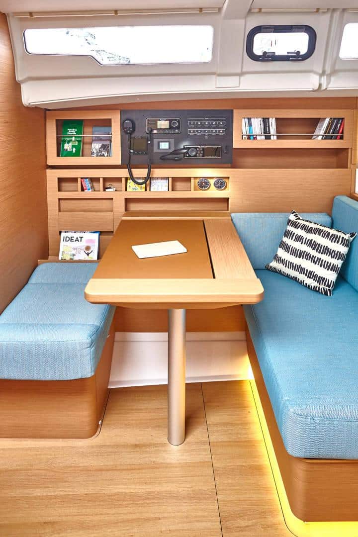 Innenansicht einer Katamaran-Kabine mit einem Holztisch, blau gepolsterten Bänken, einem Bücherregal und einer Stereoanlage unter natürlichem Licht durch eine Luke oben.