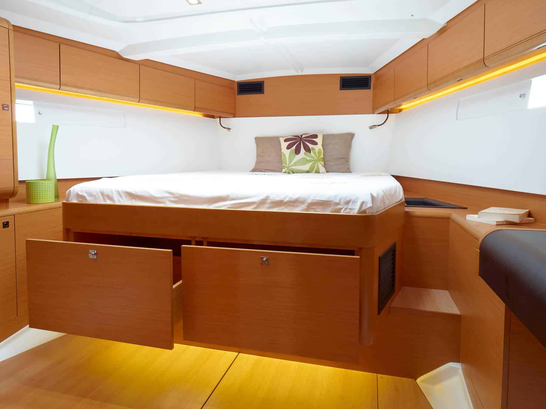Eine gemütliche Yachtkabine mit einem ordentlich gemachten Bett mit einem geblümten Kissen, umgeben von polierten Holzschränken und sanfter Umgebungsbeleuchtung, perfekt für eine entspannte Segelreise.
