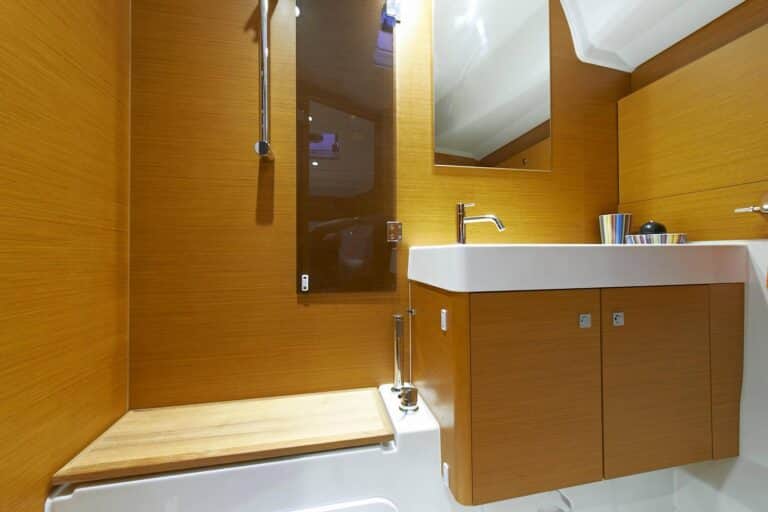 Modernes Badezimmer-Interieur mit Holzwänden, weißem Waschbecken, Spiegel und Edelstahlarmaturen auf einer Segelyacht.