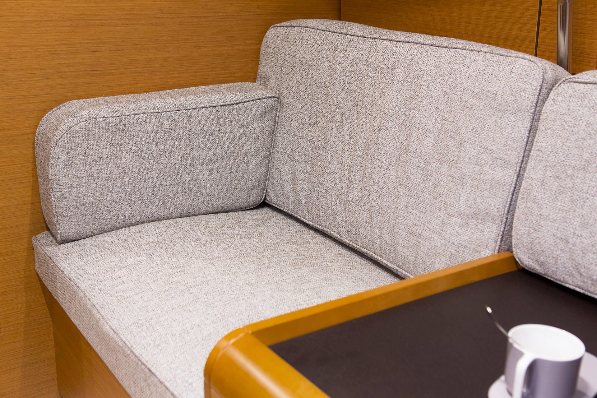 Ein modernes graues Stoffsofa mit Holzarmlehne, platziert in einer gemütlichen Ecke neben einem kleinen Holztisch mit einer weißen Tasse auf einem Katamaran.