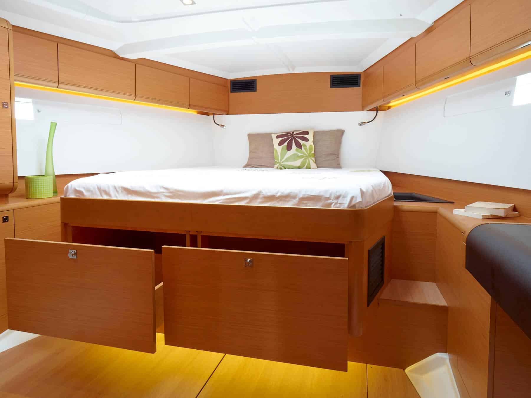 Eine moderne Segelyachtkabine mit großem Bett, Holzschränken und sanfter Beleuchtung, die ein gemütliches und luxuriöses Ambiente schafft.