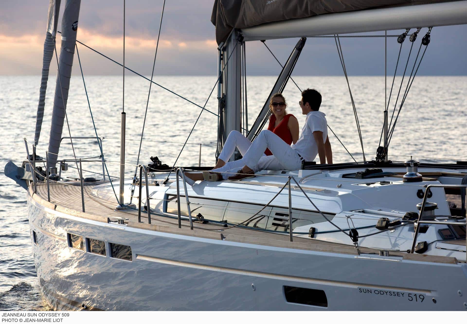 Ein Mann und eine Frau sitzen auf dem Deck einer Sun Odyssey 519-Yacht und genießen während ihres Segeltörns den Sonnenuntergang über dem Meer.