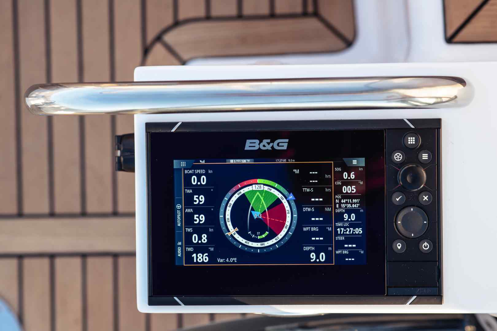 Ein modernes Schiffsnavigationsdisplay auf einer Segelyacht, das digitale Messwerte für Windrichtung, Geschwindigkeit und Bootsgeschwindigkeit anzeigt, mit einem Holzdeck im Hintergrund.