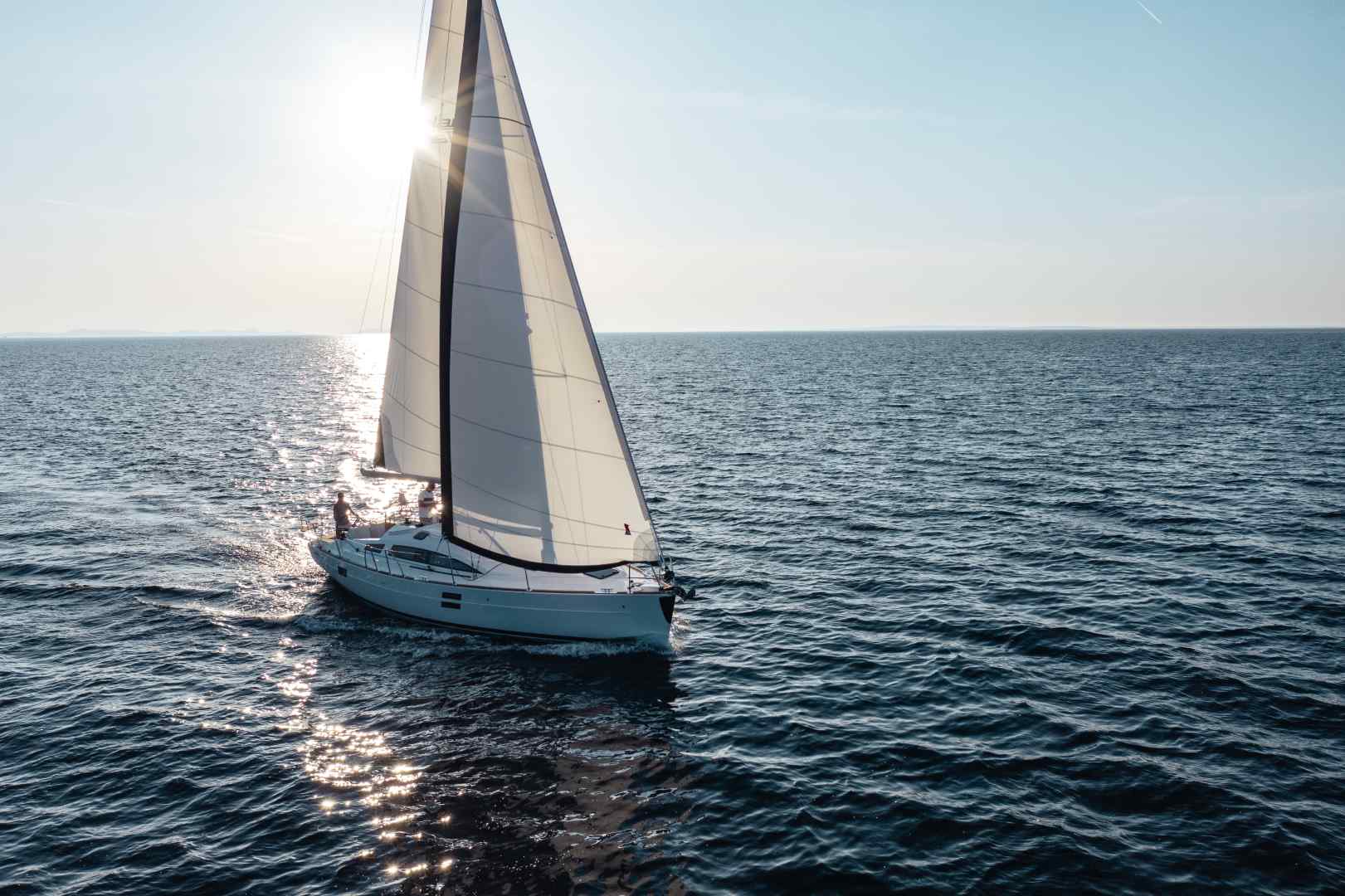 Ein Segelurlaub-Segelboot segelt auf ruhiger See unter klarem Himmel, während sich das Sonnenlicht im Wasser spiegelt.