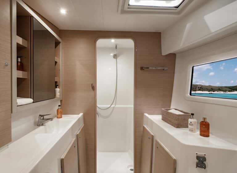 Modernes Yachtbadezimmer mit Schiebetür, Holzschränken und einem großen Fenster mit Meerblick. Neutrale Töne und gut organisierte Toilettenartikel schaffen einen sauberen, einladenden Raum. Ideal für einen Segelurlaub oder eine Segelreise.