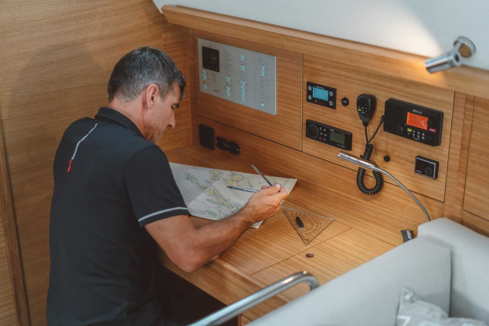 Ein Mann untersucht eine Seekarte an einem Kartentisch in der Kabine einer Segelyacht, umgeben von Navigationsinstrumenten.
