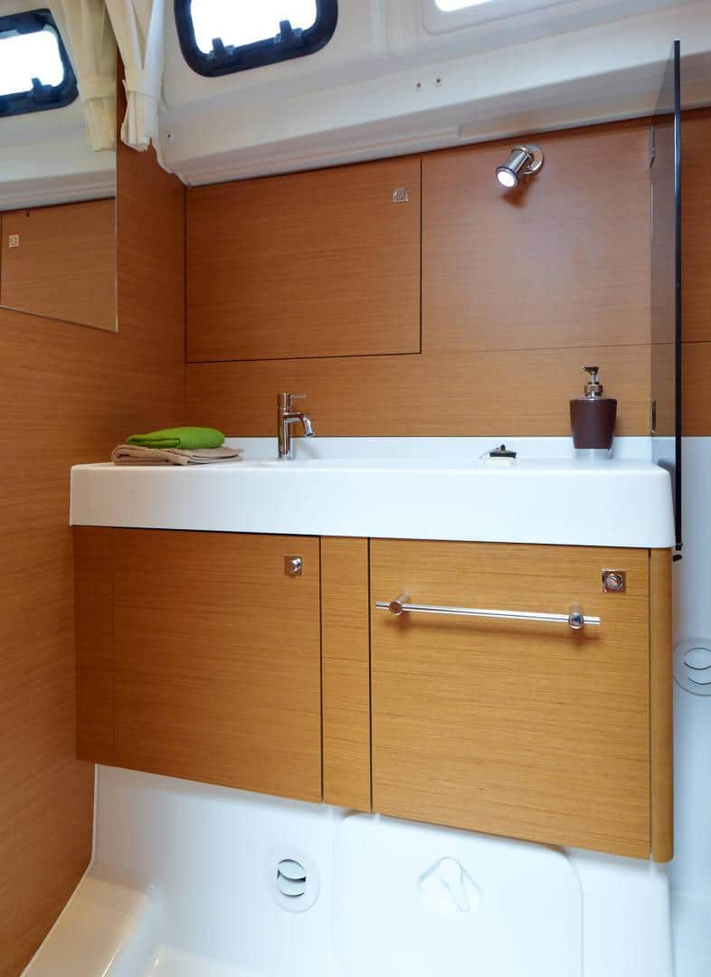 Ein modernes Bootsbadezimmer mit einem weißen Waschbecken mit Chromarmaturen, eingelassen in einen hölzernen Waschtisch mit dazu passenden Schränken und Wänden. Der Raum wird von Deckenstrahlern beleuchtet, ideal für einen Katamaran.