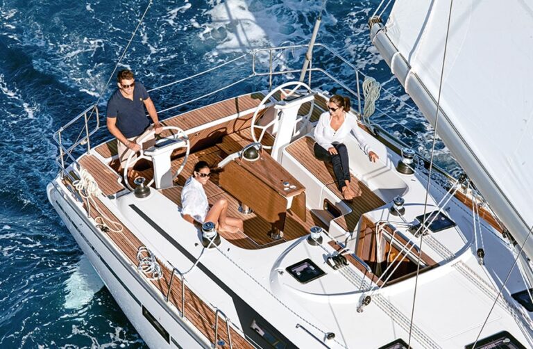 Drei Personen entspannen und steuern einen Katamaran auf dem blauen Wasser und präsentieren dabei das geräumige Deck mit Sitzgelegenheiten und Segelausrüstung.