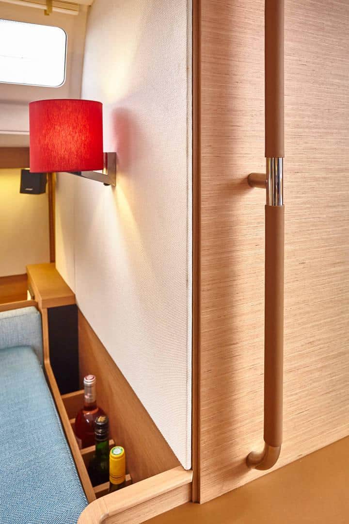 Eine gemütliche Kabinenecke mit einem roten Lampenschirm, der an einer cremefarbenen Wand über einem kleinen Nachttisch neben einem blauen Sofa angebracht ist und eine warme und einladende Atmosphäre im Katamaran-Innenraum vermittelt.