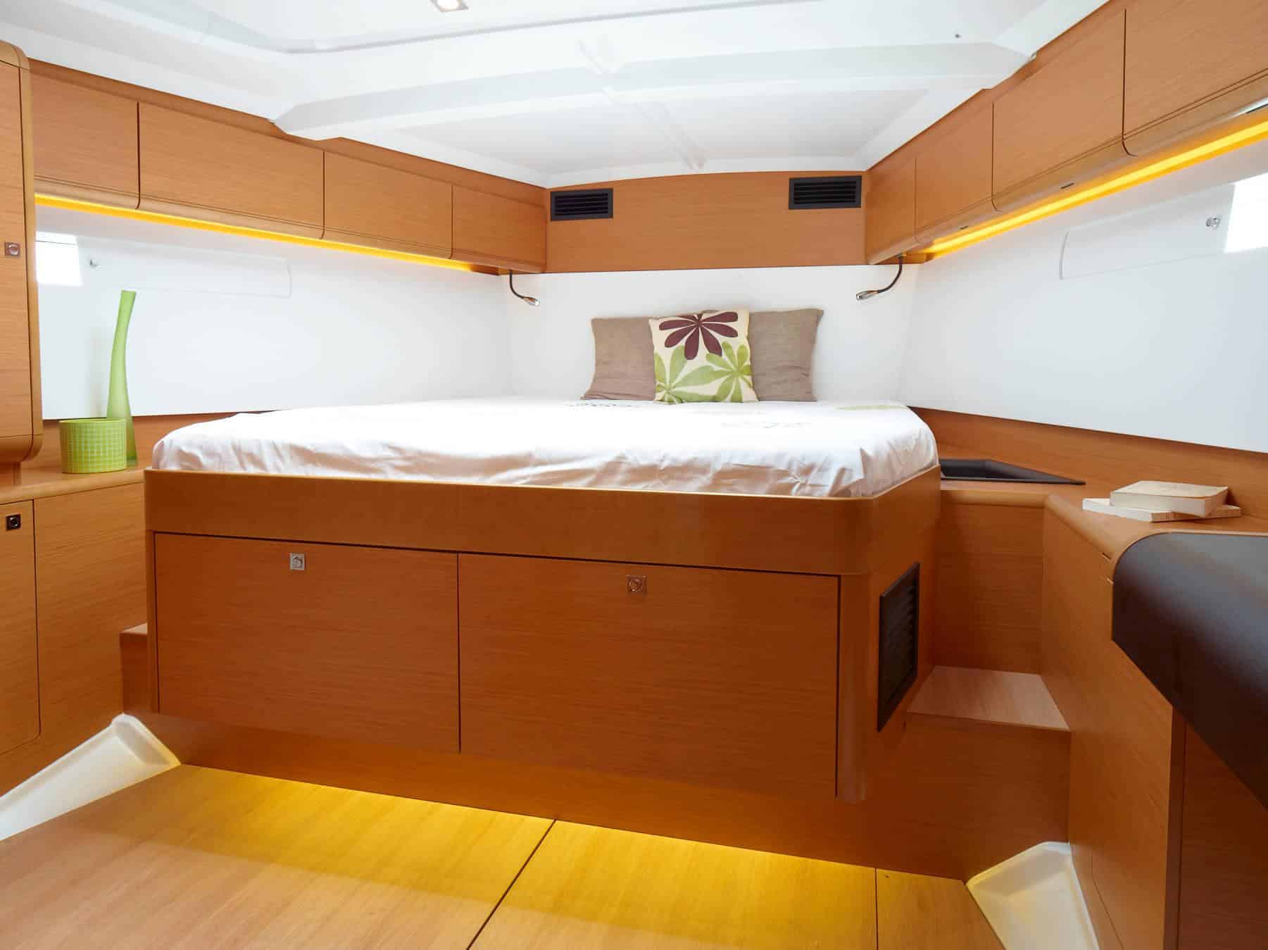 Innenansicht einer Luxus-Katamarankabine mit großem Bett mit dekorativem Kissen, Holzschränken, sanfter Beleuchtung und hellem Ambiente.