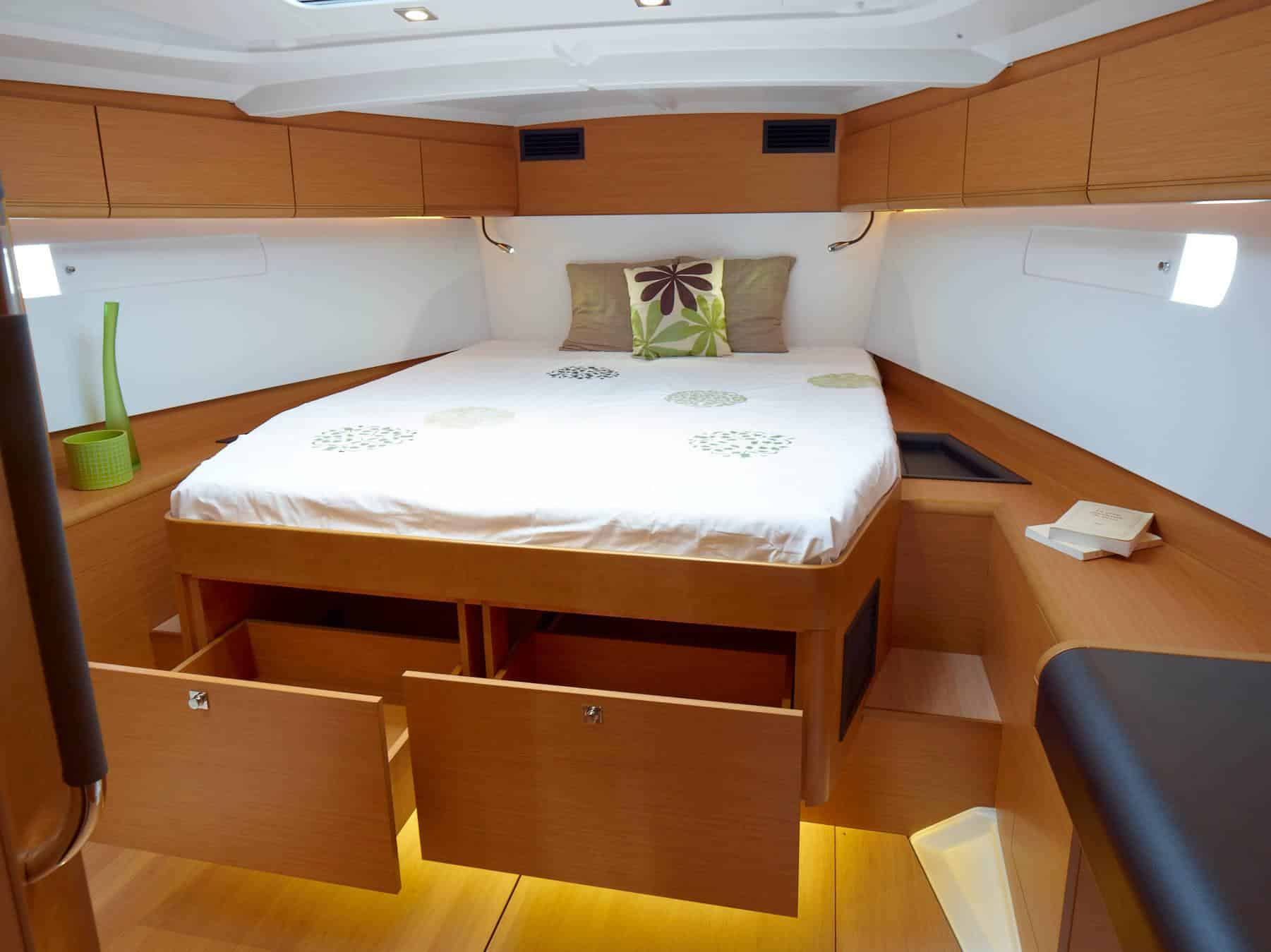 Innenansicht einer Yachtkabine mit einem sauber gemachten Doppelbett, Holzschränken und sanfter Beleuchtung. Der Raum hat ein kompaktes, modernes Design mit einem gemütlichen Ambiente, perfekt für einen Segeltörn.