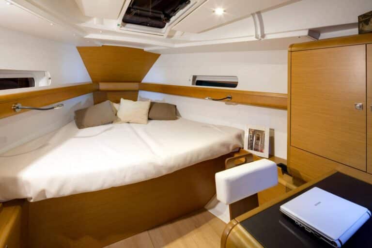 Innenansicht einer luxuriösen Katamaran-Kabine mit großem Bett, Holzpaneelen und modernen Annehmlichkeiten unter sanfter Beleuchtung.
