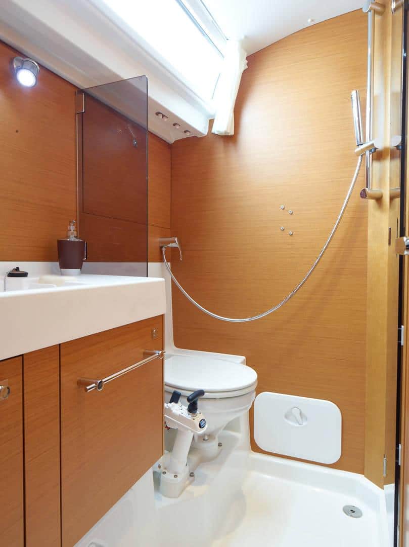 Ein kompaktes, modernes Badezimmer mit Holzwänden, einer kombinierten Dusche und Badewanne, einer wandmontierten Toilette, einem weißen Waschbecken, Schminktisch und heller Segelreise-Deckenbeleuchtung.