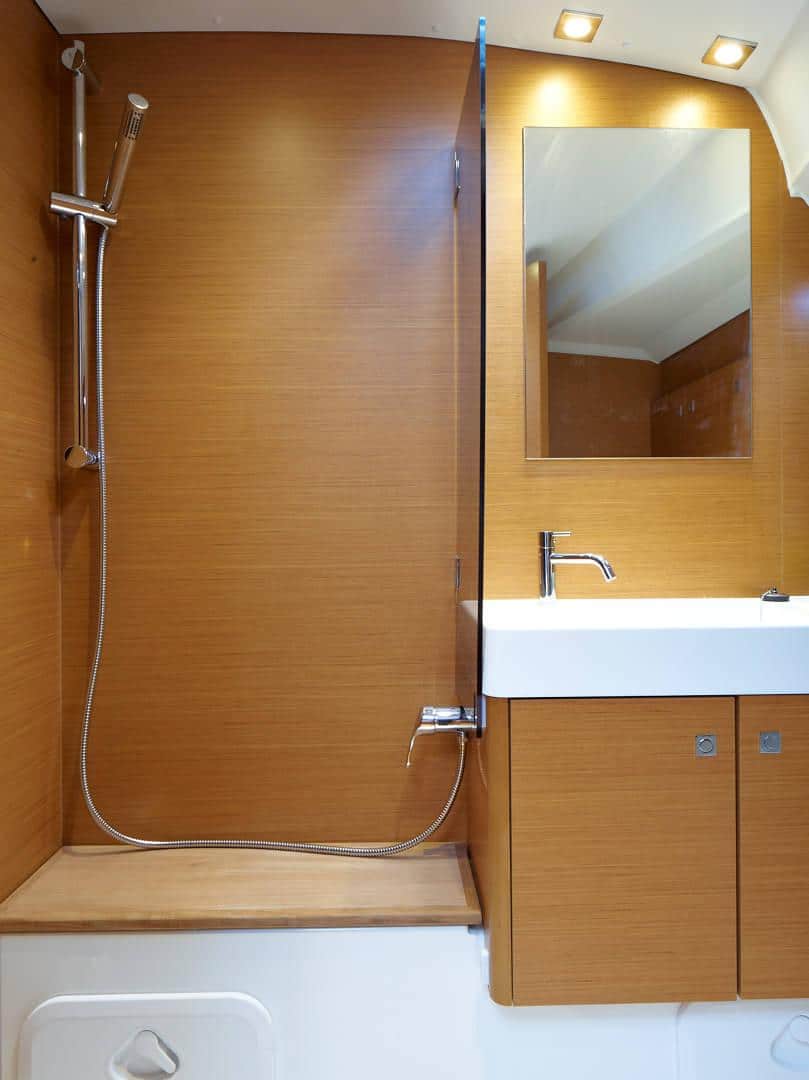 Kompaktes Badezimmer in einem Katamaran mit Holzvertäfelung, einem kleinen weißen Waschbecken mit Spiegel darüber und einer Handbrause daneben.