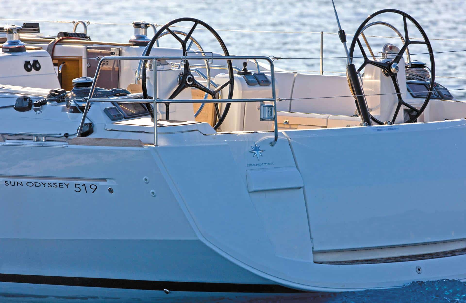 Rückansicht einer weißen Sun Odyssey 519 Segelyacht auf blauem Wasser. Zu sehen sind zwei Steuerräder und der Name des Bootes am Heck.