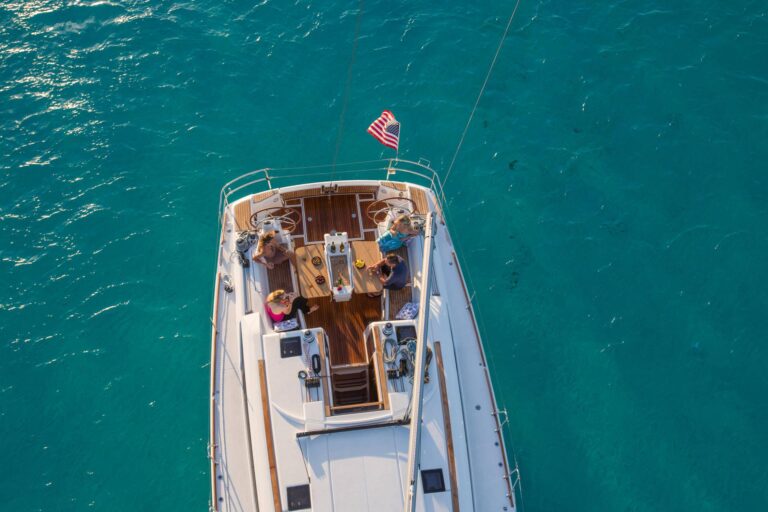 Luftaufnahme einer Gruppe von Menschen auf einem Boot mit amerikanischer Flagge, die während ihrer Segelreise einen Tag auf dem türkisfarbenen Wasser genießen. Es sind Holzdecks und Sitzbereiche sichtbar.