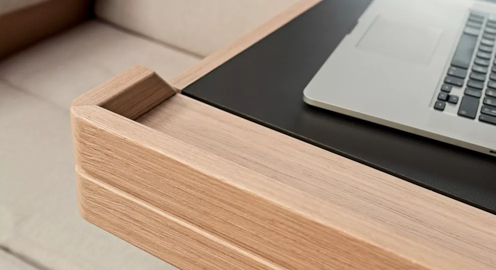 Nahaufnahme einer modernen Schreibtischecke aus Holz mit einem eleganten Laptop darauf. Die glatte Holzmaserung und das moderne Design eines Arbeitsplatzes im Katamaran-Stil werden zur Schau gestellt.