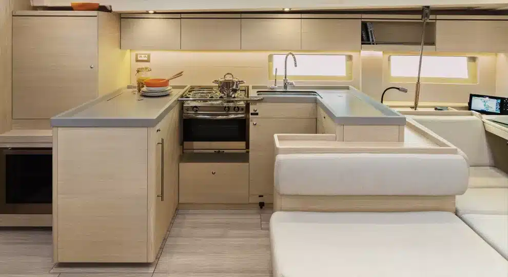 Ein modernes Segelyacht-Interieur mit einer kompakten Küche mit Herd, Ofen und reichlich Schränken neben einem weißen Sofa, alles unter warmer Beleuchtung.