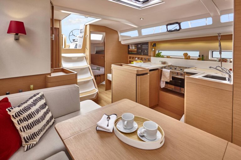 Der Innenraum des modernen Bootes, das für Yachtcharter zur Verfügung steht, bietet einen gemütlichen Sitzbereich mit einem Tisch für zwei Personen, komplett mit Tassen und Untertassen auf einem Tablett. Der Raum ist mit Holz verkleidet, hat eine angrenzende Kombüsenküche und eine Treppe, die zu einem Oberdeck mit sichtbaren Fenstern führt.