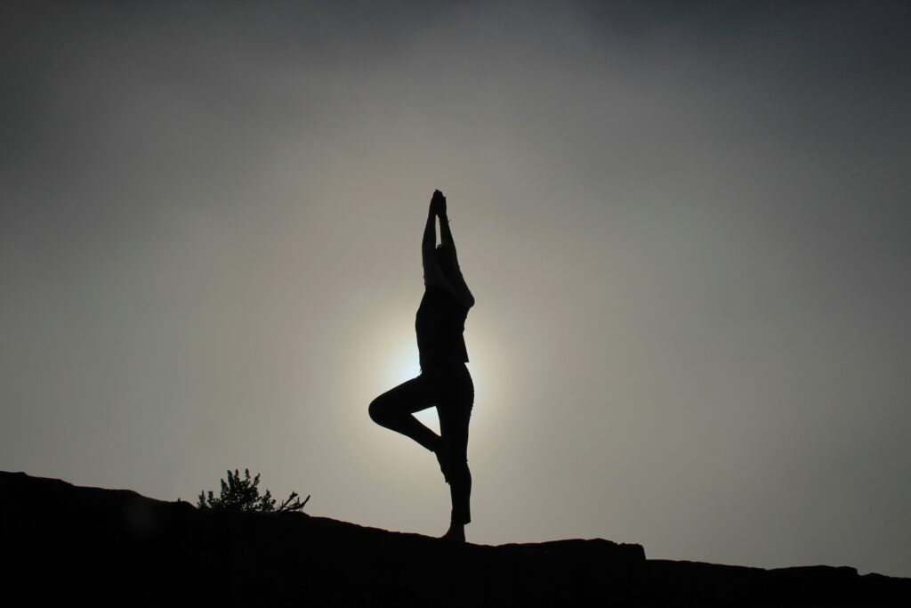 Eine ruhige Silhouette einer Person, die vor dem Hintergrund einer sanft leuchtenden Sonne auf Mallorca die Baumstellung im Yoga ausführt.