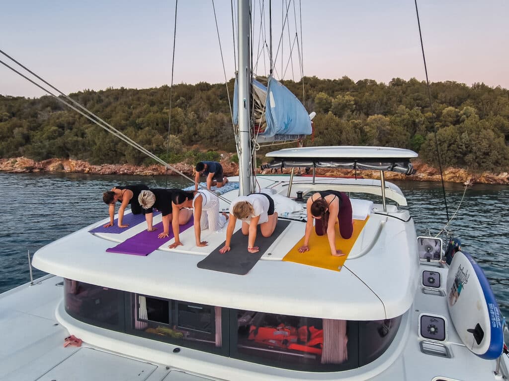 A woman practising yoga on the deck of a catamaran in a calm bay