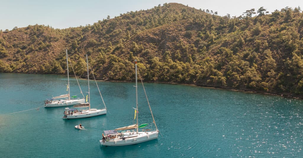 Three white sailing yachts anchored in a calm turquoise Turkish bay