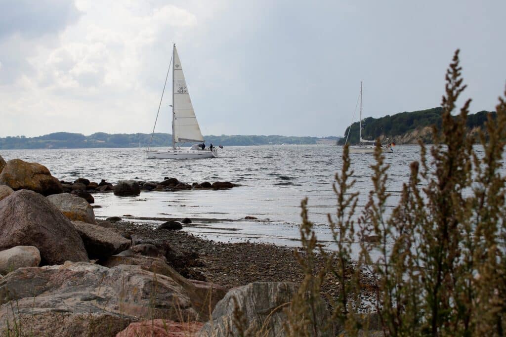 Weißes Segelboot auf grauer Ostsee vor Steinküste – segeln ostsee sailwithus