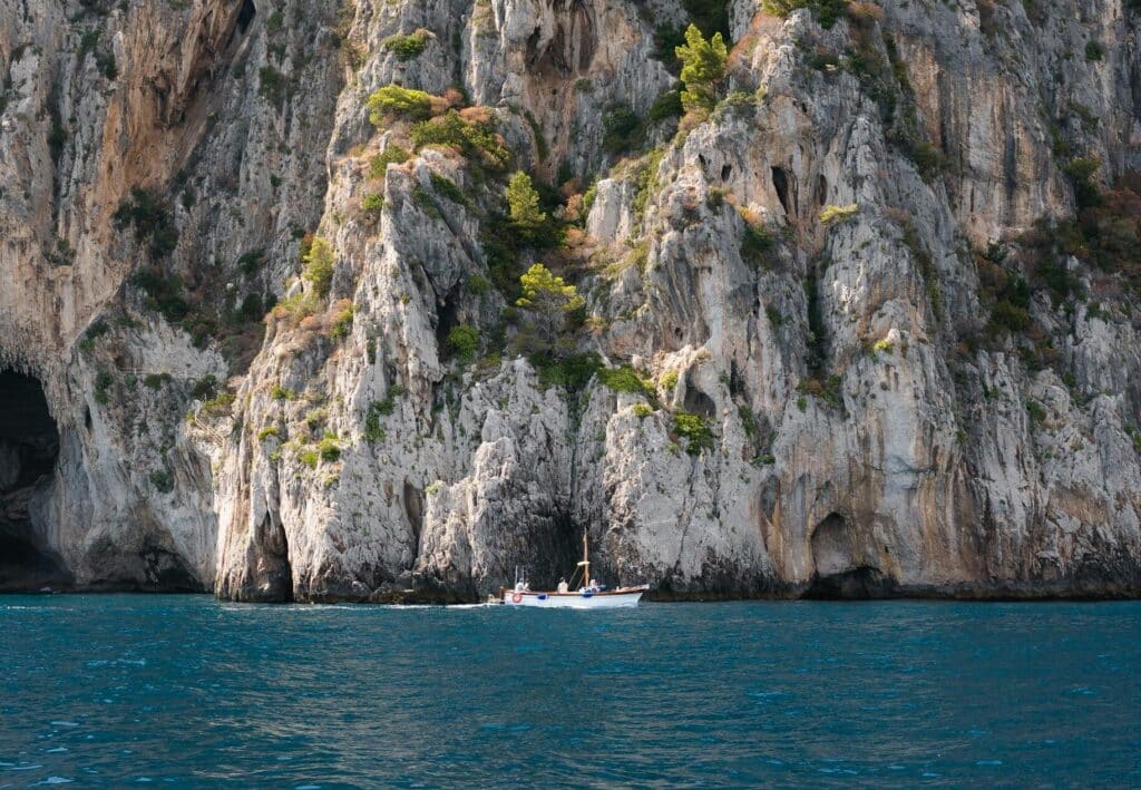 Dominant rocky cliffs of Capri Island with a small boat on the blue ocean waters. Amalfiküste