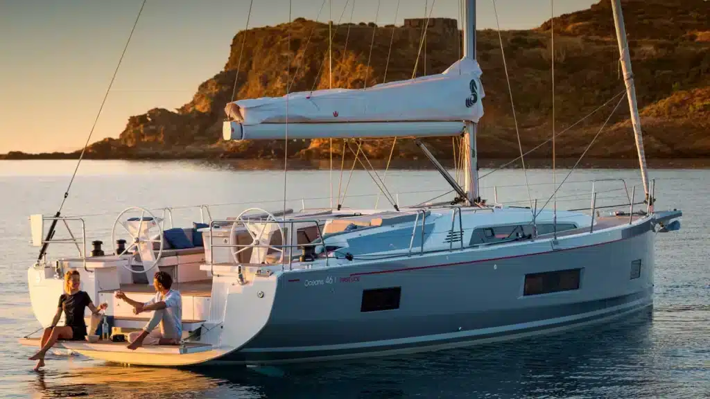 Paar sitzt auf Heckplattform Beneteau Oceanis 46 und trinkt Champagner bei Sonnenuntergang sailwithus