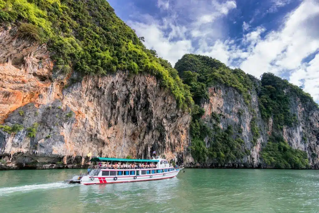 A boat cruise offers breathtaking views of lush cliffs under a bright blue sky.