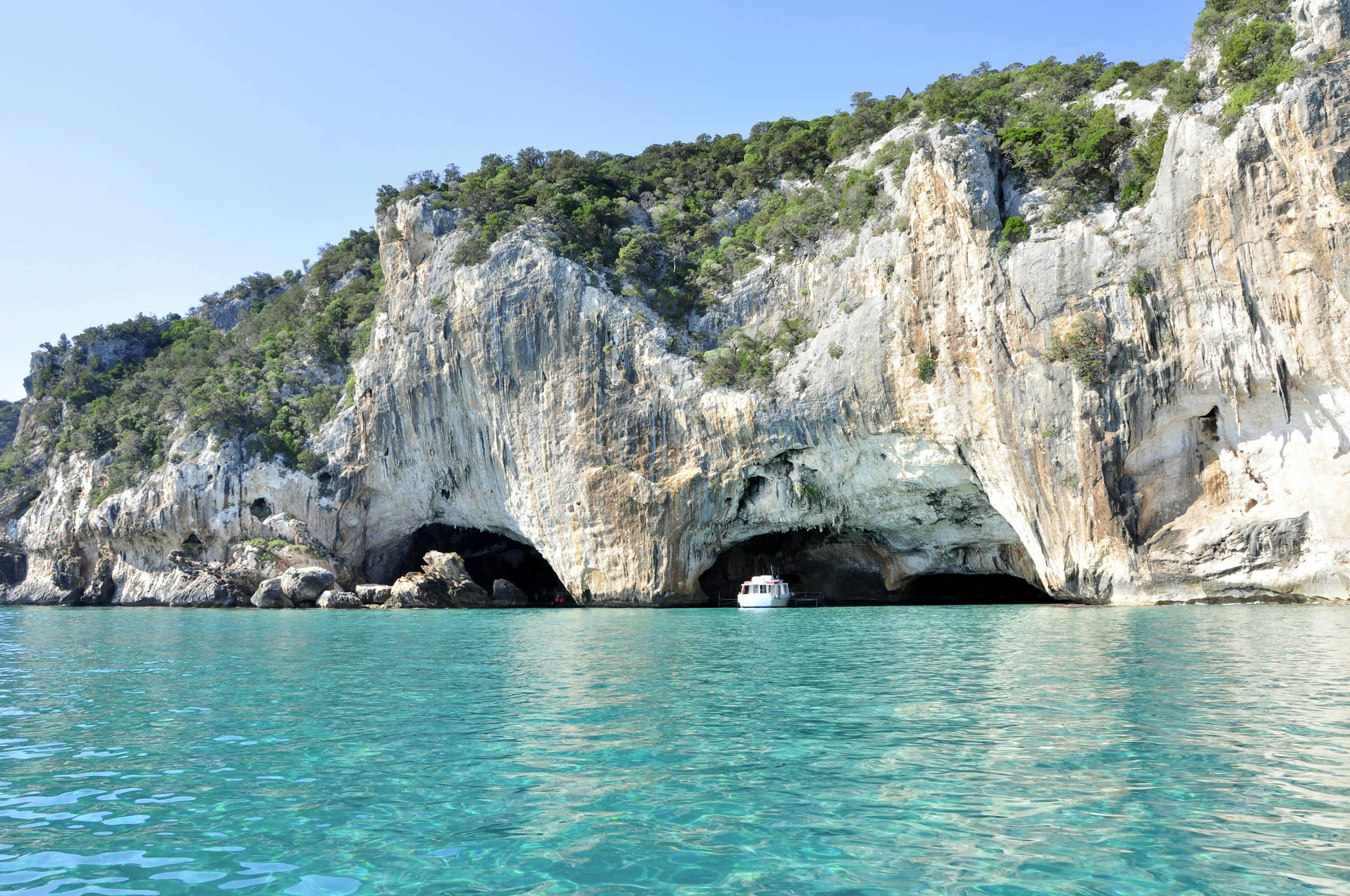 A boat enters a stunning cave along the rocky coastline of the Mediterranean Sea. Sardinien