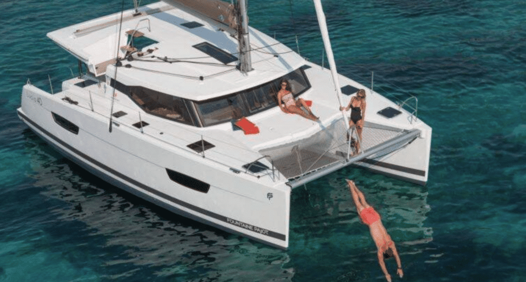 Young sailors jumping off a catamaran into the sea on a sunny sailing trip